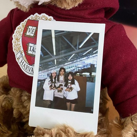 A Harvard bear holding an instant photo of Orey and two friends in Harvard sweatshirts.