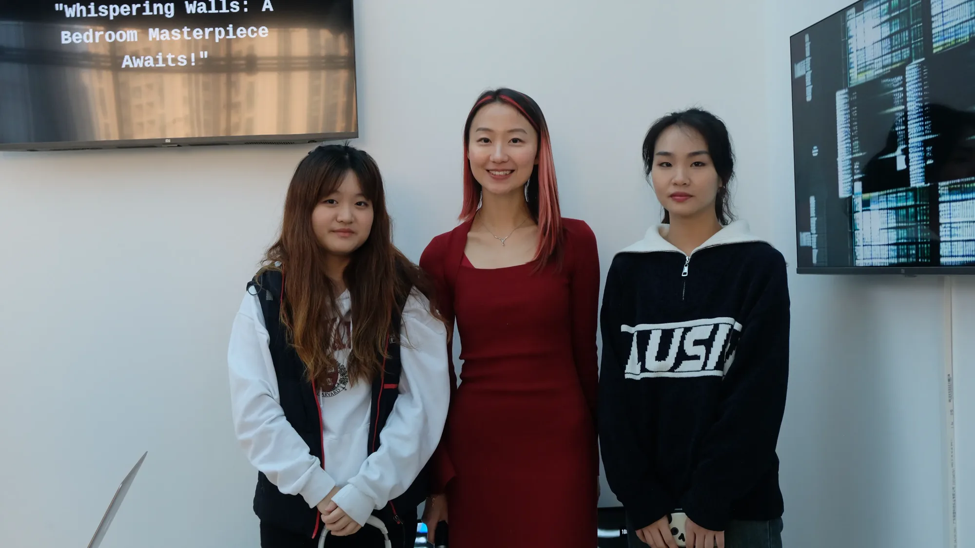 Three members of the team standing together at the exhibition, in front of a white wall with two screens.